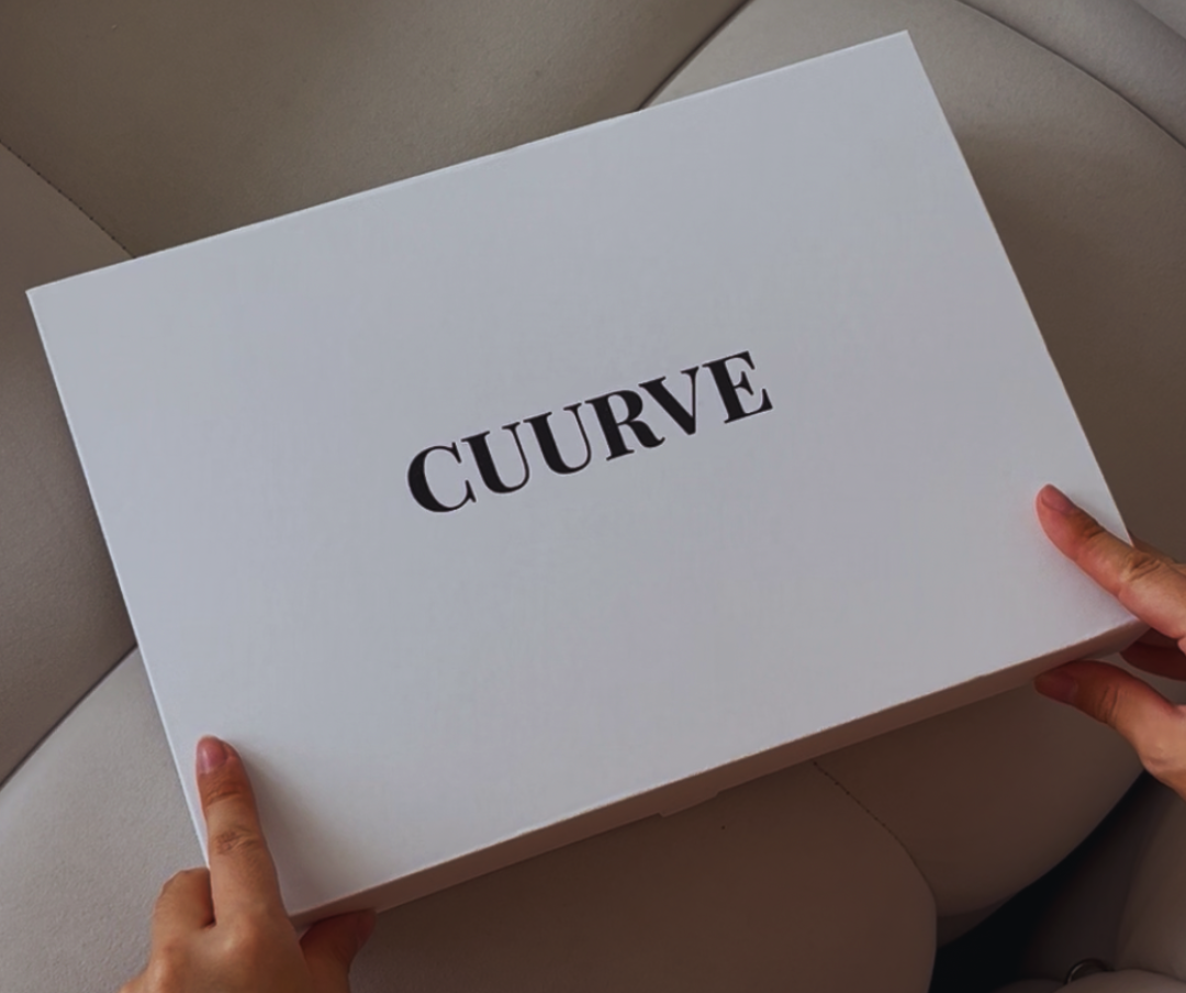 White box with 'CUURVE' branding held by a person on a beige couch.