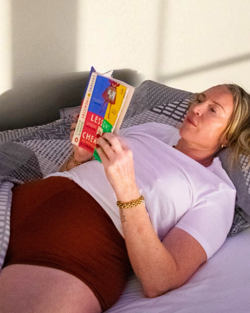 Woman lying in bed reading a book, wearing Cuurve Cosy Charlotte terracotta comfort shorts.