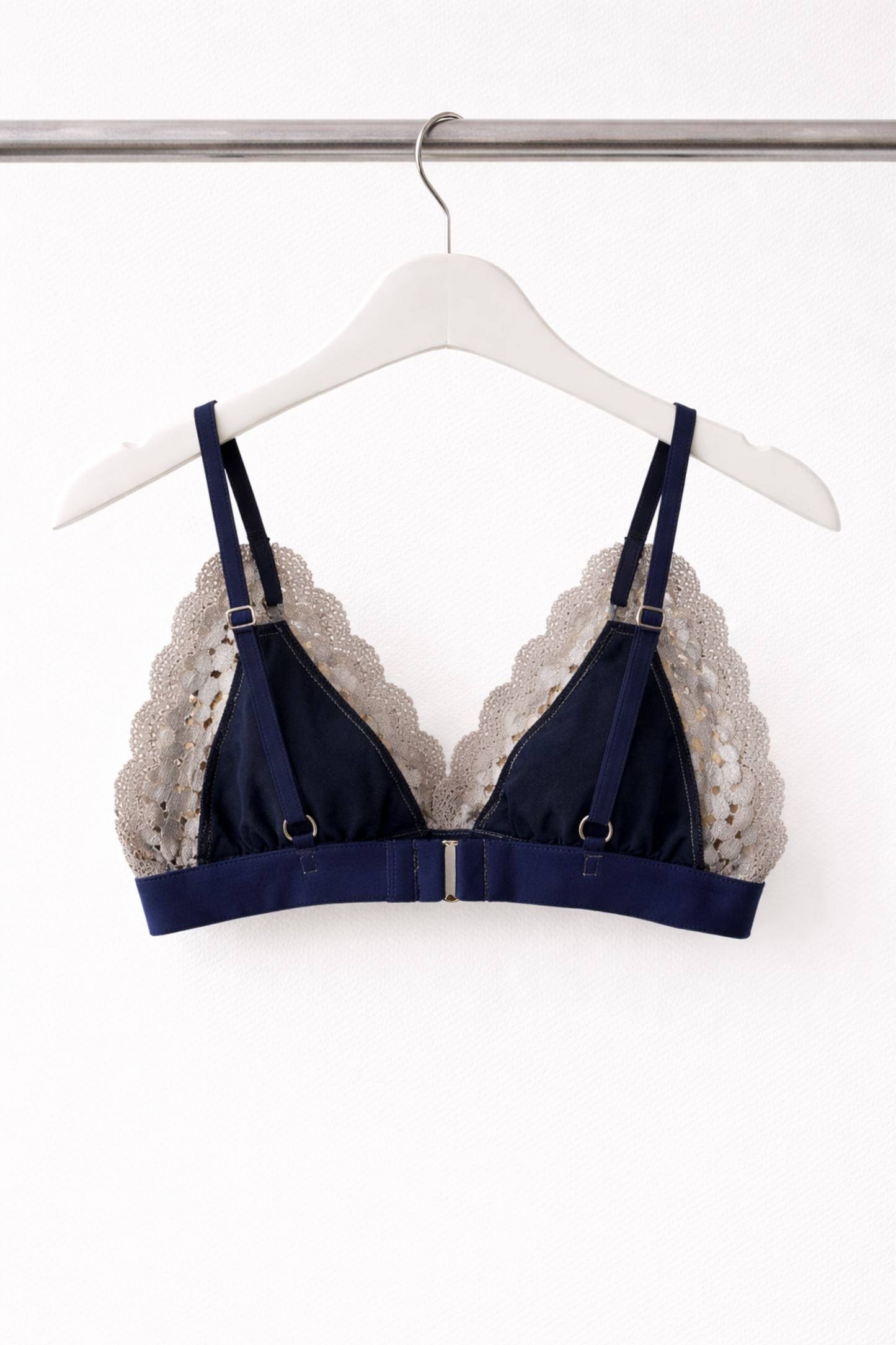 Back view of an airy navy wire-free lace bralette showing adjustable straps, gold hardware, and a soft underband, displayed on a white hanger.