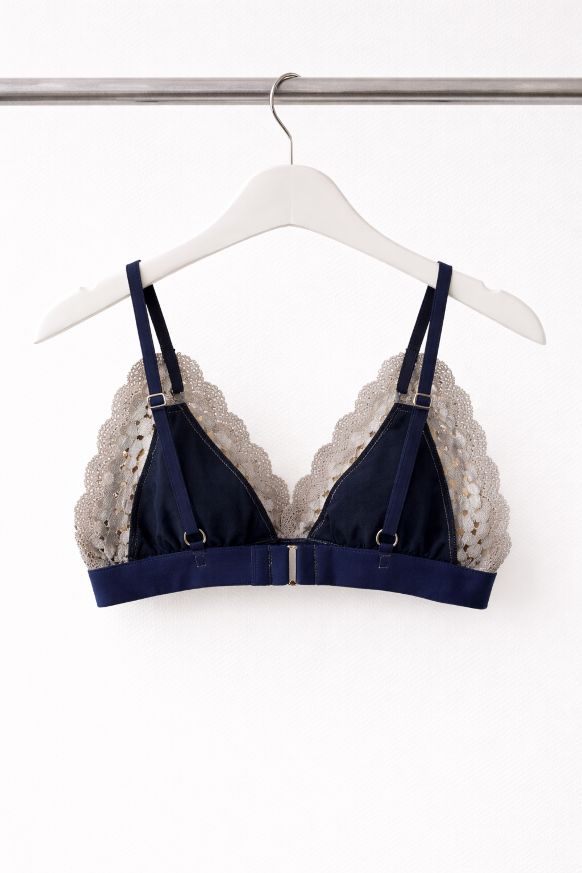 Back view of an airy navy wire-free lace bralette showing adjustable straps, gold hardware, and a soft underband, displayed on a white hanger.