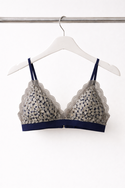 Airy navy wire-free lace bralette with soft triangle cups, shown hanging on a white hanger against a neutral background.