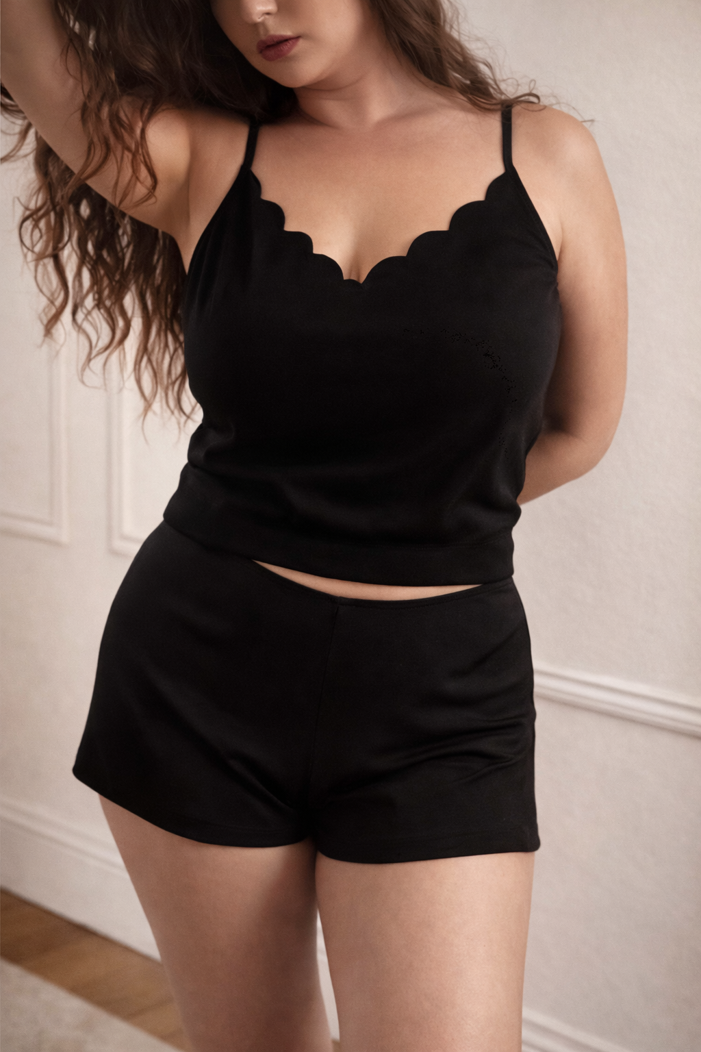 Woman wearing a black lace-trimmed top and shorts against a neutral background