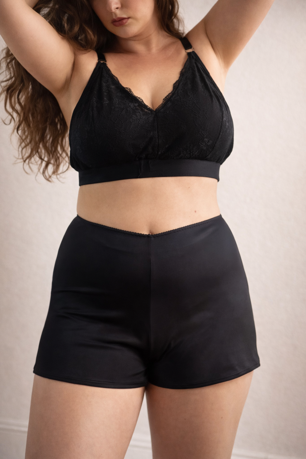 Person wearing a black lace bralette and high-waisted shorts against a neutral background