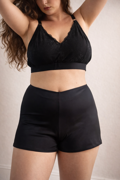 Person wearing a black lace bralette and high-waisted shorts against a neutral background