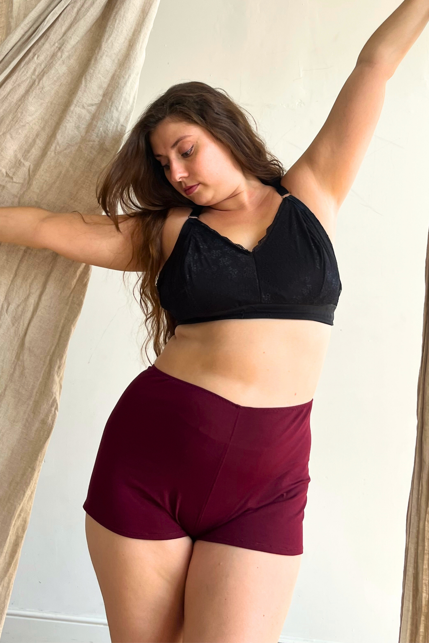 Woman wearing a black sports bra and maroon shorts against a neutral background