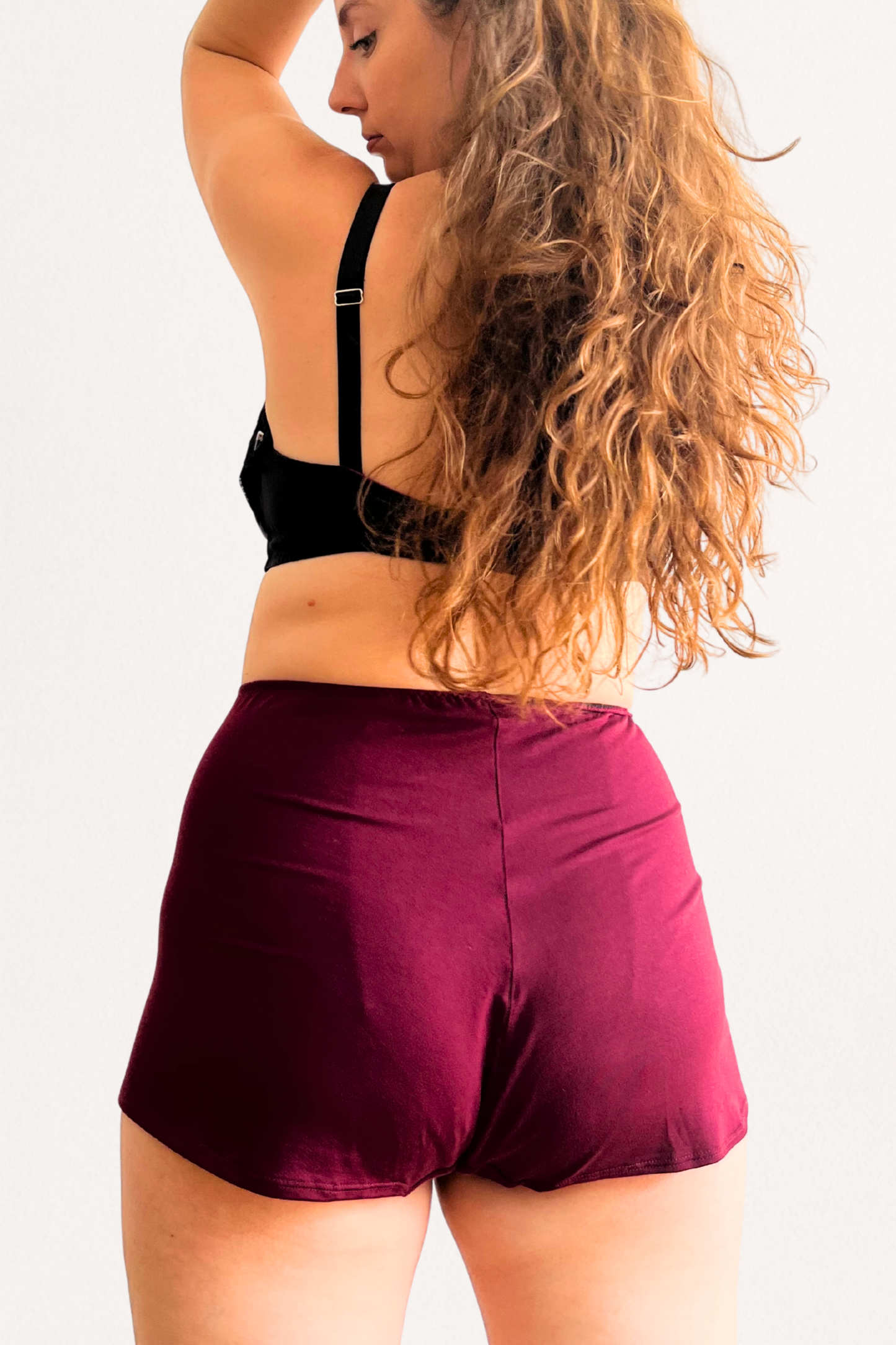 Person wearing a black sports bra and burgundy tencel modal shorts on a white background