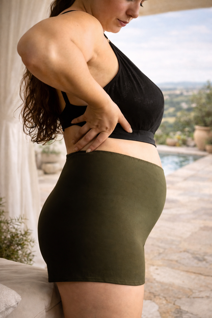 Woman wearing a black top and green skirt outdoors with a pool and garden in the background