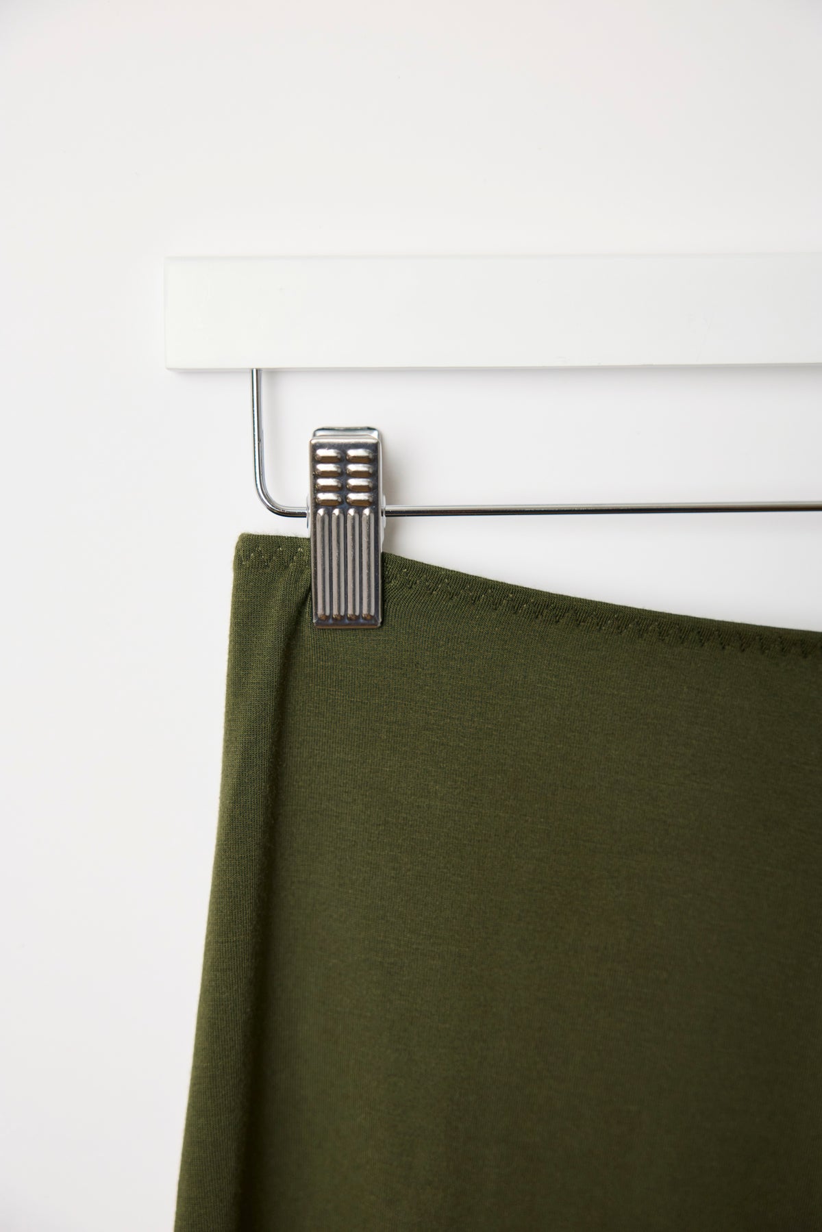 Close-up of the dark olive fabric and hanger clip, showing the waistband hem detail