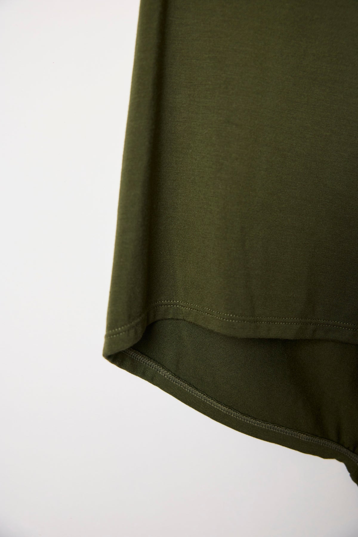 Close-up of the dark olive shorts' curved hem seam and fabric texture