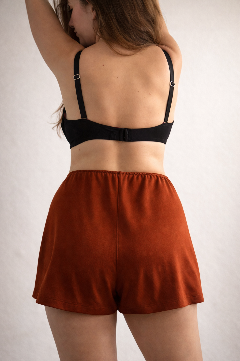 Person wearing a black bra and rust-colored shorts on a plain background