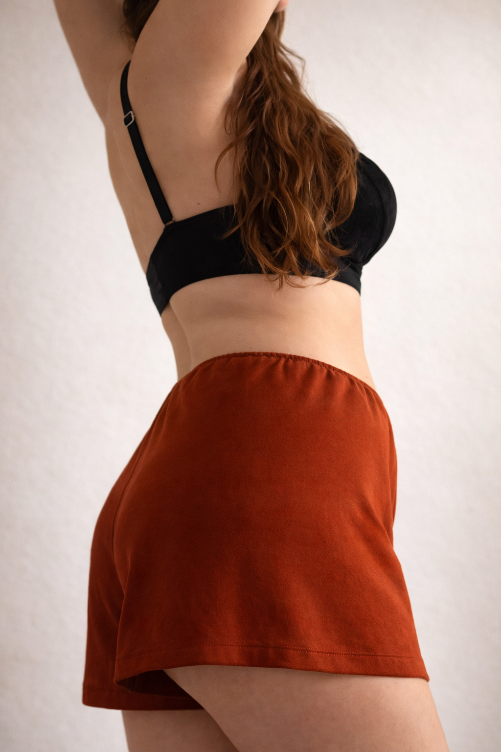 Person wearing a black bra and rust-colored skirt on a white background