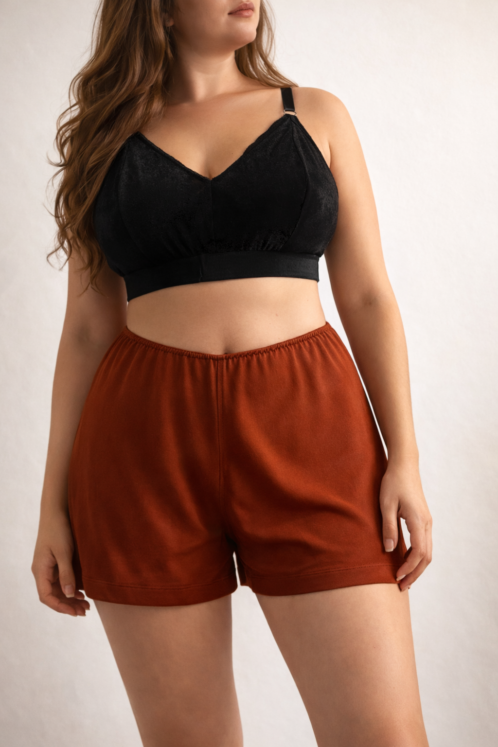 Woman wearing a black crop top and rust-colored shorts on a plain background