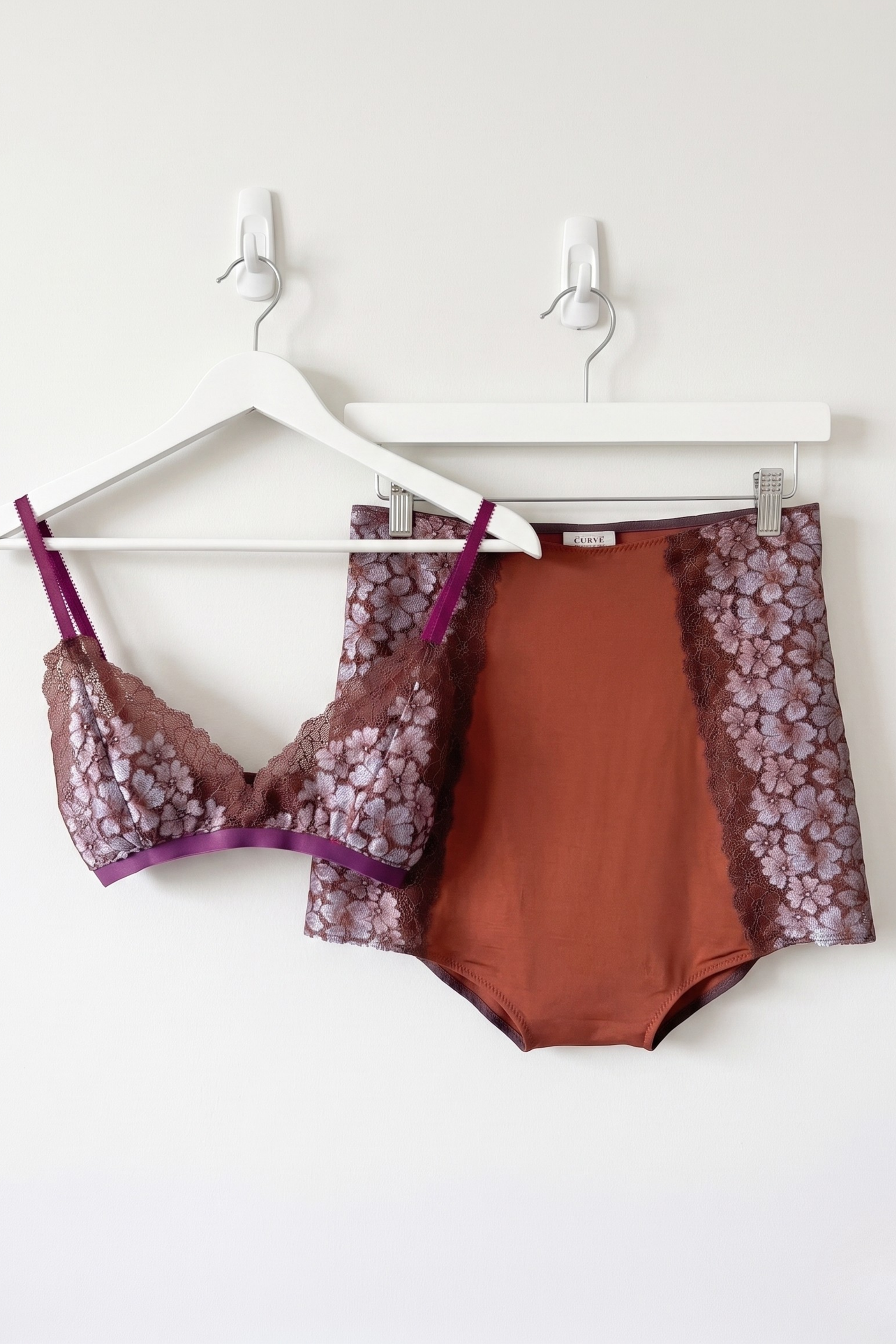 Bralette and high rise pants hanging on hooks on a white wall 