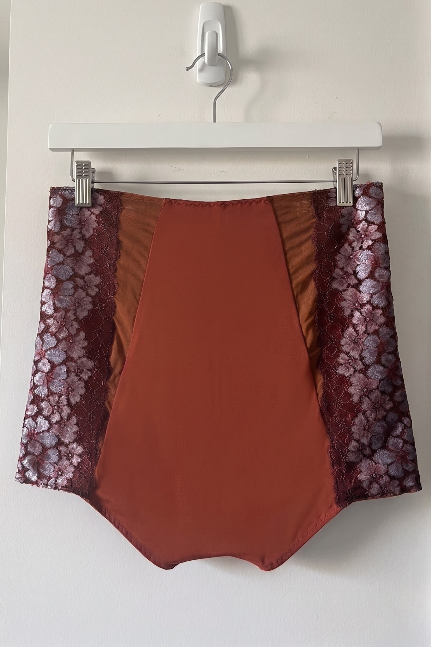 Brown high rise pants with floral lace trim on a white hanger against a white wall