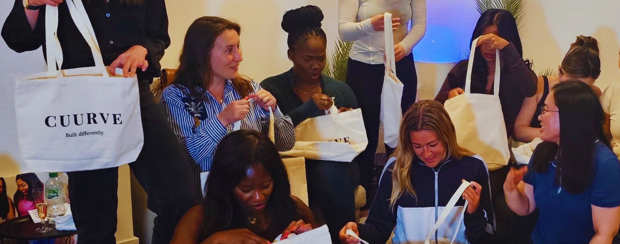Group of people gathered around, opening and interacting with 'CUURVE' bags.