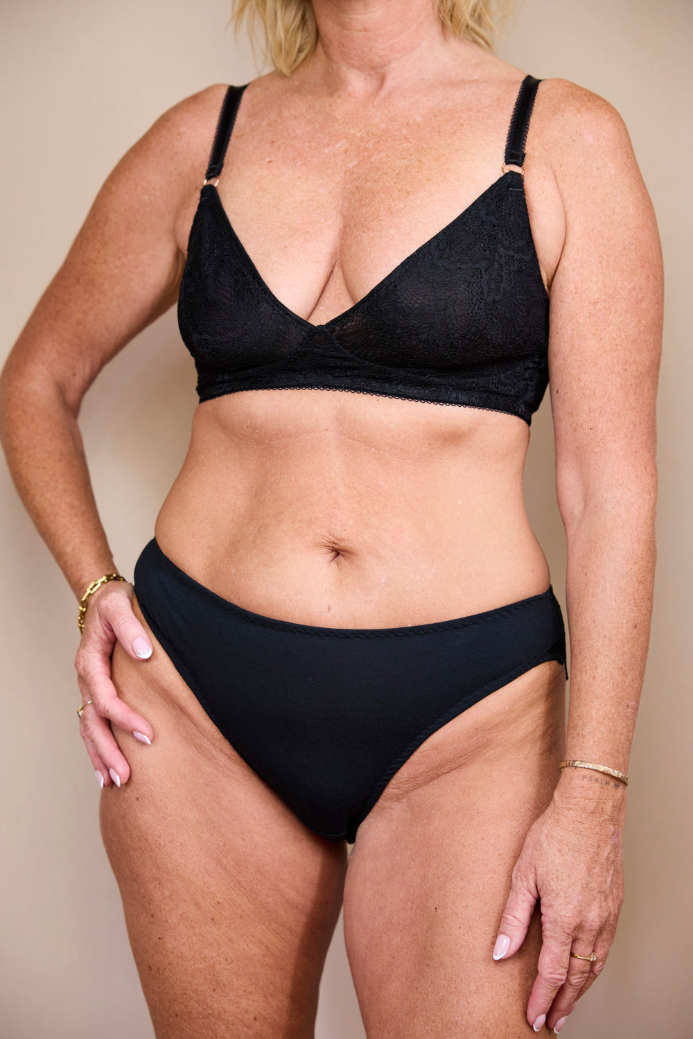 Woman wearing a black low-rise brief and matching lace bralette, front view