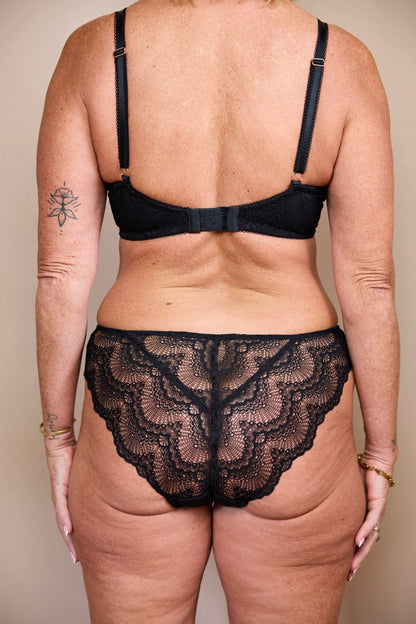 Straight-on back view of a woman wearing a black bralette and low-rise brief with lace back panel