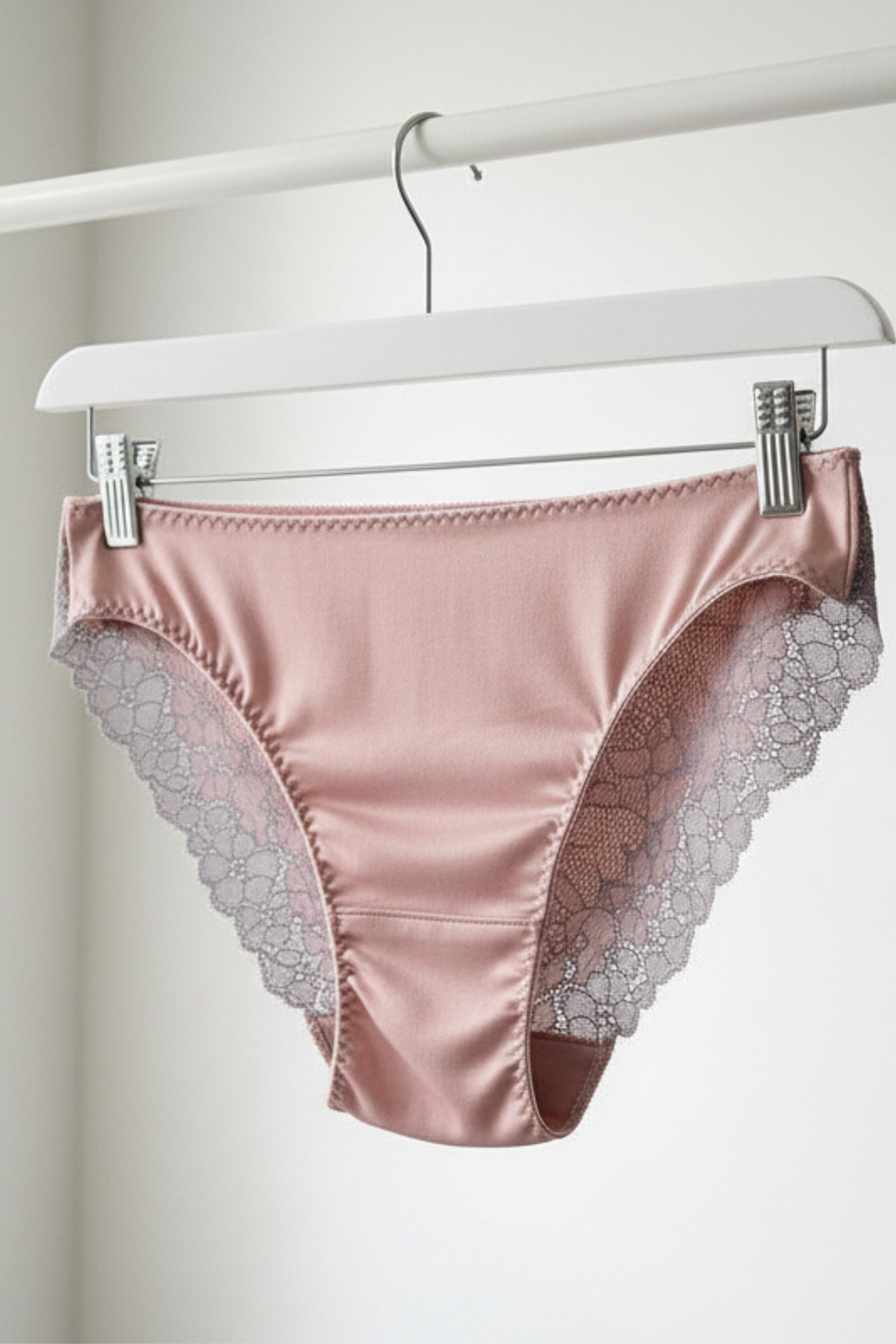 Handcrafted UK lingerie brief in blush pink, soft rose and silver dawn lace, Cuurve Sleek Sophie, front view hanging on rail in natural light