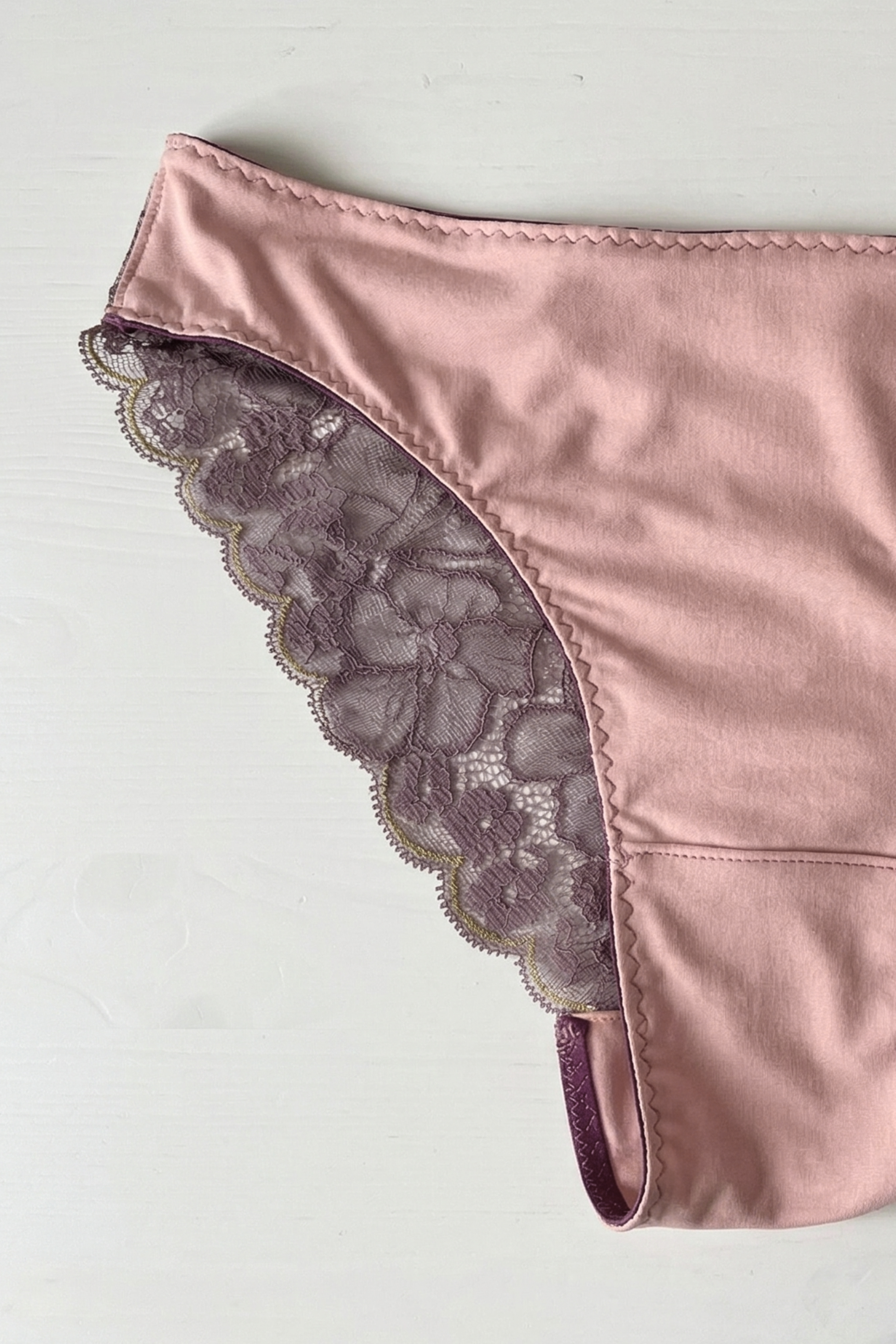 Handcrafted UK lingerie brief in blush pink and dusk lace, deep violet lace with gold trim detail, Cuurve Sleek Sophie,flat lay on a white table showing the trim detail 