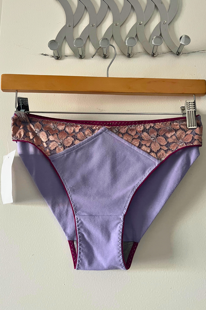 cinderella panty in lilac cotton jersey with metallic rose lace panel and fuchsia elastic, displayed on a hanger against a clean white background.