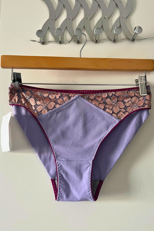 cinderella panty in lilac cotton jersey with metallic rose lace panel and fuchsia elastic, displayed on a hanger against a clean white background.