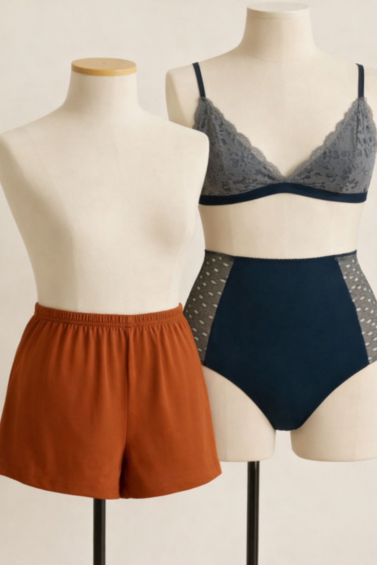 Mannequins displaying the Cosy Charlotte rust-colored comfort shorts and the Elevated Emma navy high-rise brief with lace bralette, on a neutral background.
