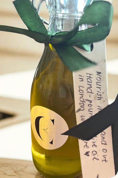 Close-up of Nikolaos extra virgin olive oil bottle from Crete tied with green ribbon and Cuurve tag — symbol of natural nourishment behind the Olive Gift Set