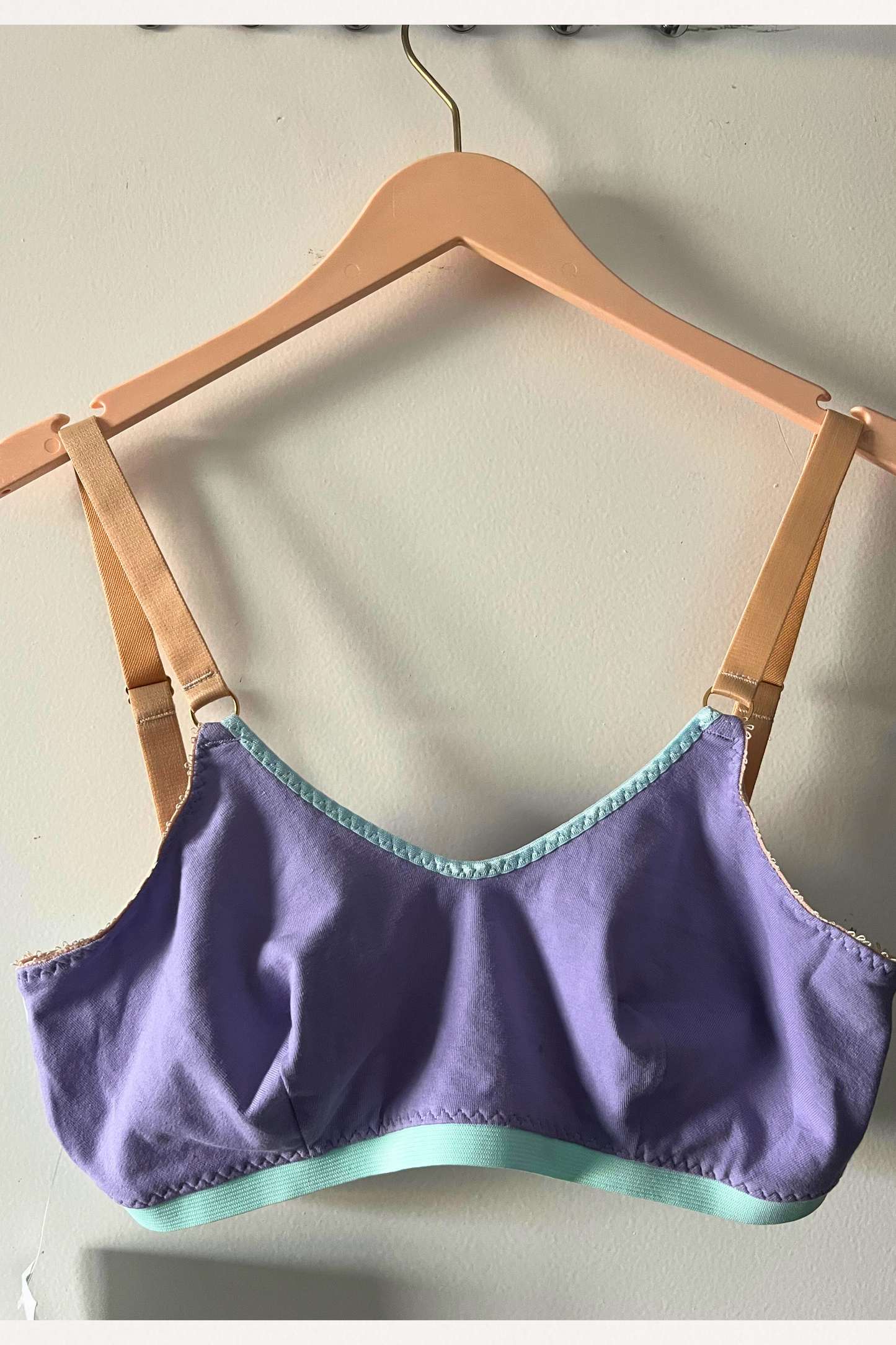 front view of the lilac and aqua round-neck bralette on a wooden hanger, showing the smooth neckline and cotton jersey cups.