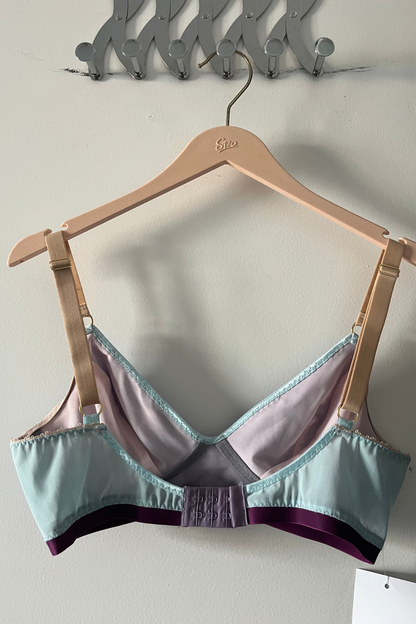 back view of the lilac and aqua v-neck bralette on a hanger, showing the hook-and-eye closure, soft straps and colour-block design.