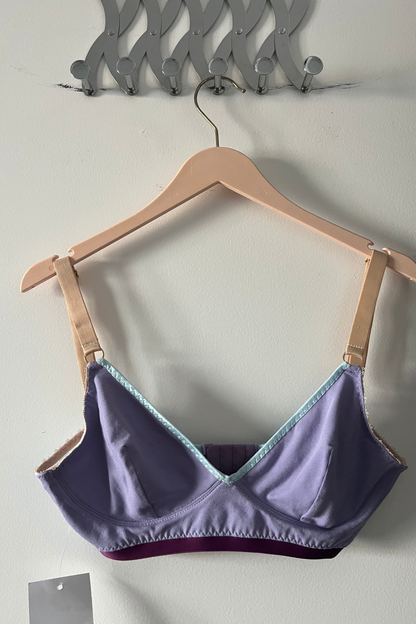 front view of the lilac and aqua v-neck bralette on a wooden hanger, showing the cup shape, aqua mesh panels and cradle construction.