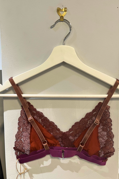 back view of the hand-sewn metallic cocoa and lilac lace bralette on a white hanger, highlighting the rose-gold hardware, soft lace texture and j-hook closure.