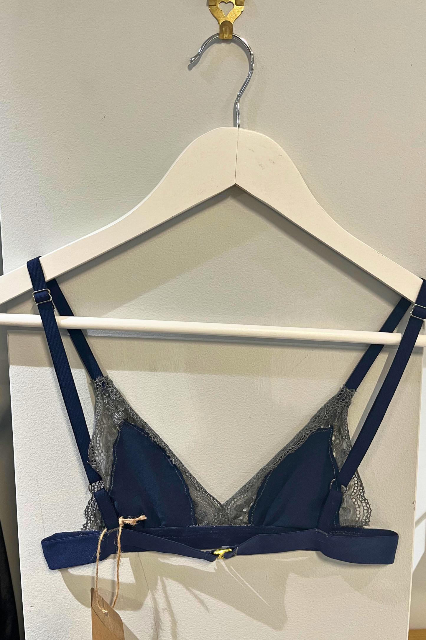 back view of the hand-sewn navy lace bralette on a white hanger, highlighting the gold hardware, lace texture and soft cup shape.