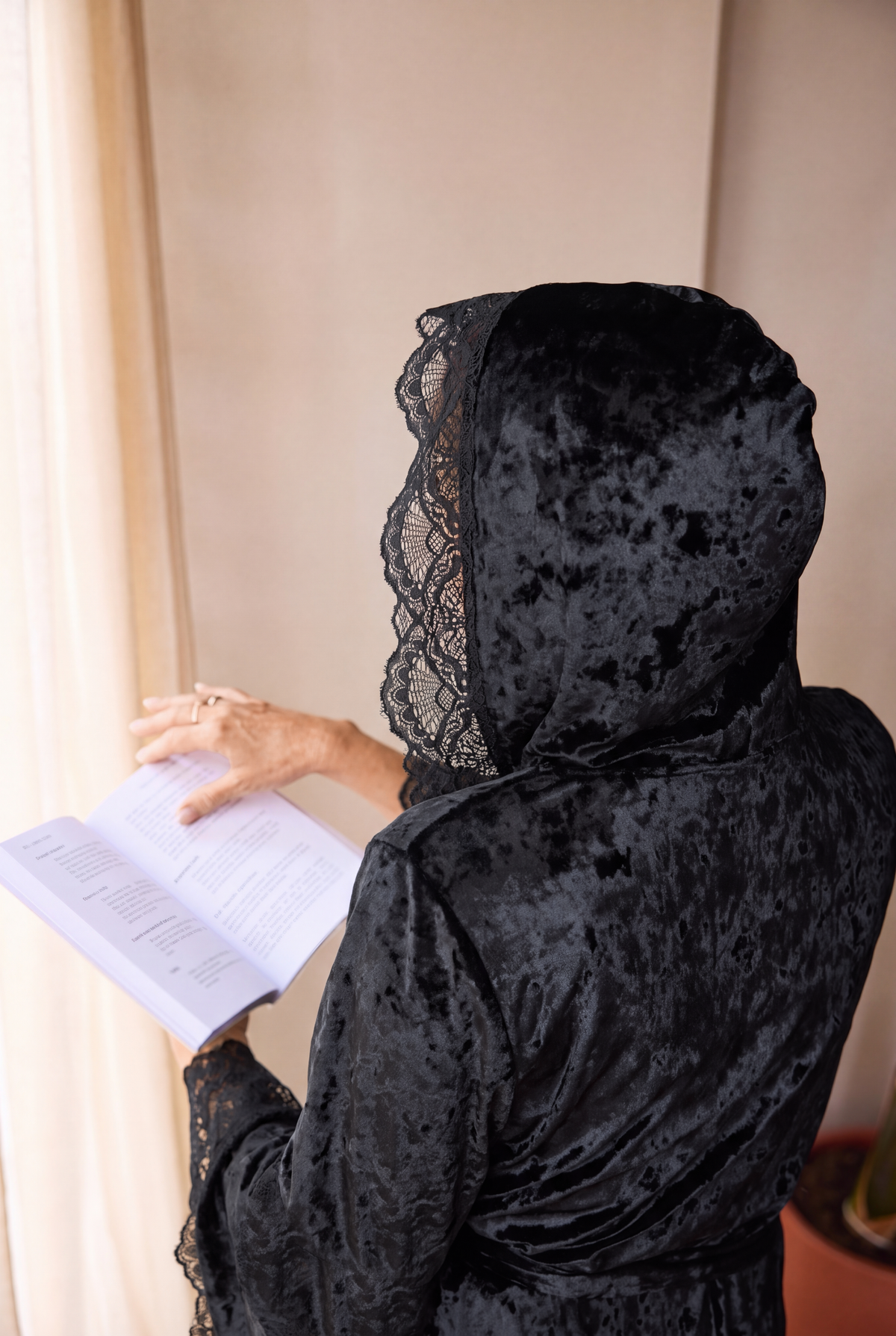 Back view of the romantasy gown with the lace-edged hood up, reading a book