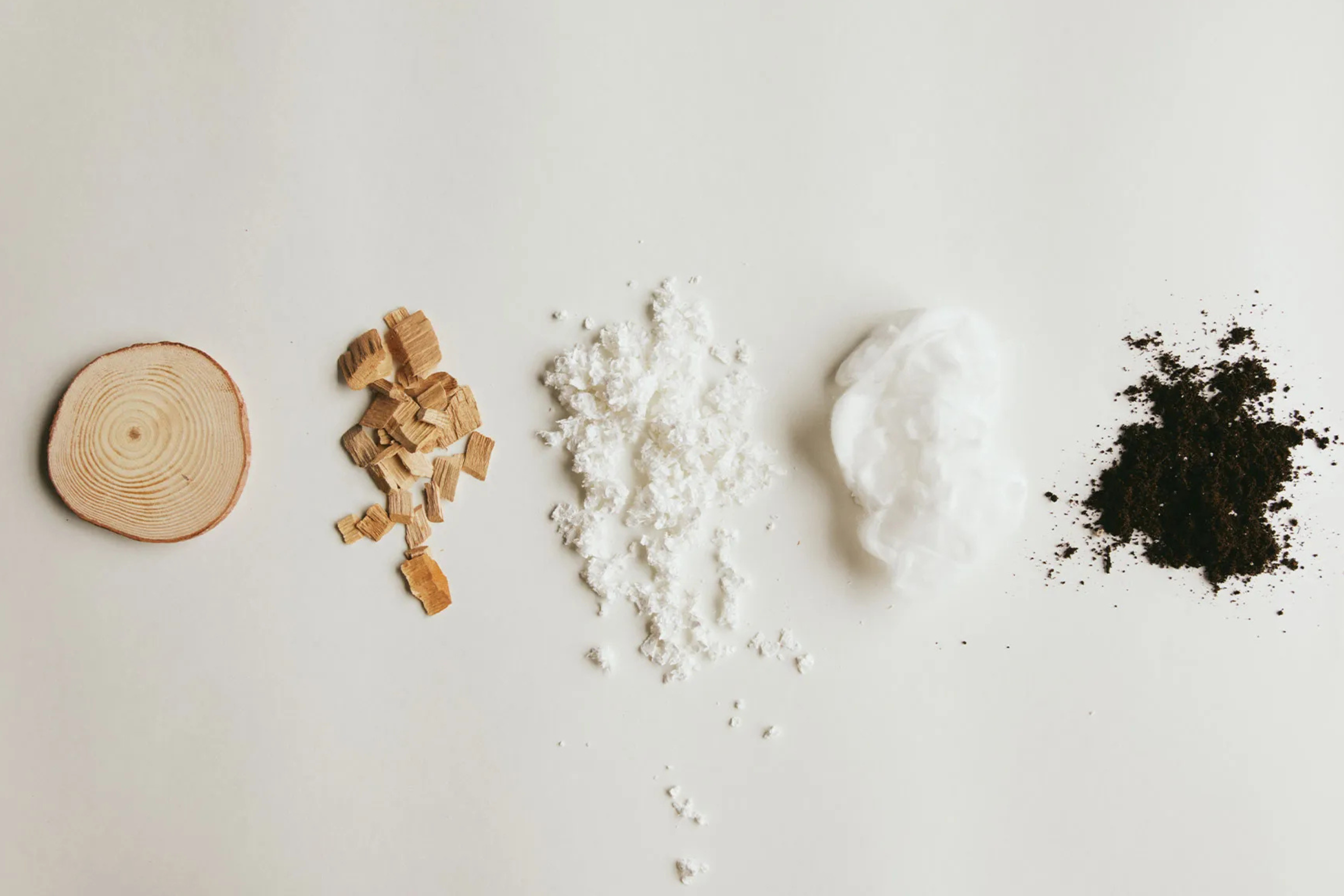 “Five natural materials showing the TENCEL™ Lyocell fibre production process — from wood log to wood chips, cellulose pulp, white fibre, and final biodegradable material — displayed on a clean white background.”